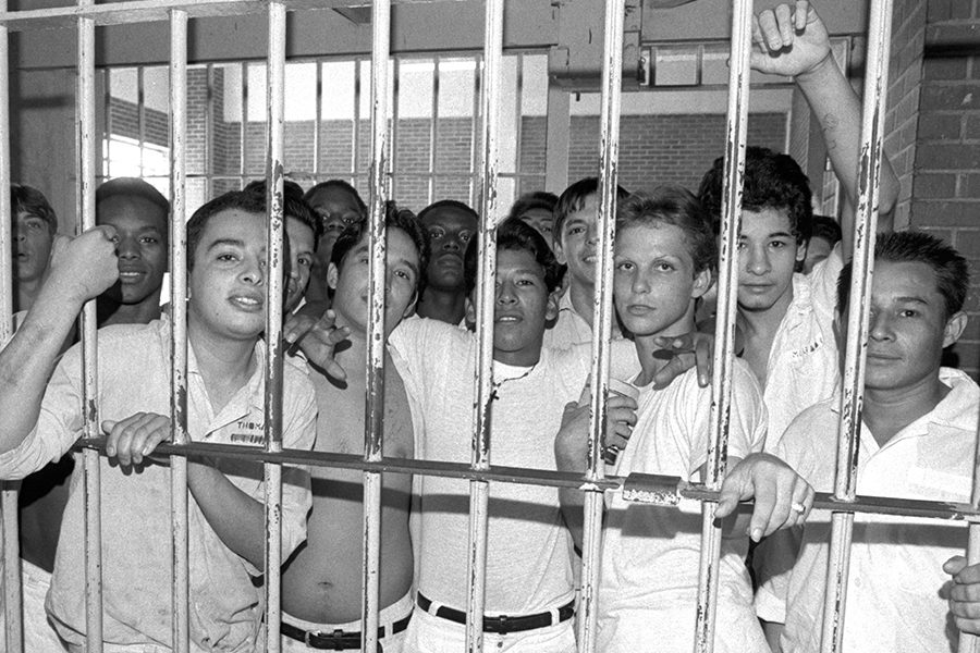 B&W photo: Young men prisoners look out cell bars.