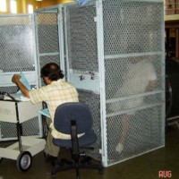 Clinician seated by open door of small holding cage with one prisoner inside