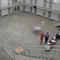 View from above of correctional officer escorting prisoner in handcuffs in dayroom