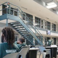 Male prisoners in dayroom, mostly seated at tables