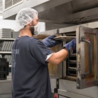 Kitchen worker removes tray from industrial oven