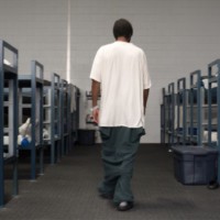 A detainee walks between two rows of dorm beds